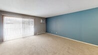 Located at 3641 Lancaster Ln N in Plymouth, MN, this single-floor unit offers a practical and functional layout spread across several distinct living areas. The spacious living room serves as the central gathering space, featuring plush carpeting, a bold blue accent wall, and a large sliding glass door fitted with vertical blinds that allows abundant natural light to fill the room. A wall-mounted air conditioning unit and baseboard heating ensure year-round climate control.

An adjacent area transitions seamlessly into a dining or secondary living space, finished with durable wood-style plank flooring and topped with a ceiling fan with light fixture. This area connects to the kitchen, which is partially visible and provides convenient access to additional storage.

The bedroom is generously sized, carpeted, and features a large window with views of the surrounding neighborhood. Baseboard heating keeps the space comfortable, and neutral gray walls create a clean, versatile backdrop.

The bathroom is accessed through a solid wood door and features tile flooring, a full tub and shower combination with a dark-toned curtain rod, and white fixtures throughout. The layout is efficient and well-appointed.

Overall, the unit presents a straightforward, livable design with a neutral color palette, ample natural light, and practical amenities throughout.