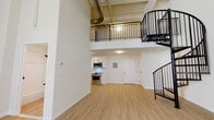 Located at 57 Cannon St in Poughkeepsie, NY, this two-floor loft-style unit blends industrial character with modern finishes throughout. The main level immediately impresses with soaring double-height ceilings that amplify the sense of openness, light hardwood flooring, and crisp white walls. Exposed ductwork overhead nods to the building's industrial heritage, while large windows invite abundant natural light into the generous living area. A striking black spiral staircase serves as both a functional and architectural centerpiece, connecting the main level to the upper loft, which features black metal railings overlooking the space below. The kitchen is thoughtfully appointed with white shaker cabinetry, stone-look countertops, a classic subway tile backsplash, a stainless steel deep-basin sink, and stainless steel appliances including an electric range and over-the-range microwave. The bathroom showcases refined design details, including floor-to-ceiling herringbone white tile, matte black fixtures, a soaking tub, and a white vanity with a framed mirror. Baseboard heating runs along the perimeter of the living areas, ensuring year-round comfort. The upper level provides additional versatile living or sleeping space, completing this well-designed urban loft.
