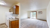 Located at 3401 E 11th St in Sioux Falls, South Dakota, this two-bedroom, one-bathroom unit offers a practical and comfortable single-floor layout. The galley-style kitchen is well-equipped with warm wood cabinetry lining both sides, laminate countertops, white appliances including a range and refrigerator, and durable tile flooring. The kitchen flows directly into a combined dining and living area, where plush carpet, baseboard heating, and a textured ceiling create a cozy atmosphere. The spacious living room is highlighted by a sliding glass door that opens to a private balcony, filling the space with natural light and outdoor views. Both bedrooms are carpeted and feature ceiling fans with light fixtures, large windows with vertical blinds that invite natural light, and generous closet storage — with three closets total throughout the unit. The full bathroom includes a tub-shower combination with a clean white surround. Baseboard heaters are present throughout the unit, ensuring consistent warmth. A dedicated hallway connects the living spaces to the bedrooms and bathroom, contributing to a well-organized and functional floor plan. The textured ceilings are consistent throughout, adding a classic residential character to the overall space.
