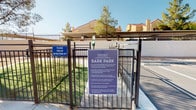 The Element Bark Park is a thoughtfully designed outdoor amenity tailored specifically for dogs and their owners. Enclosed by sturdy iron fencing, the park provides a secure environment where registered pets can roam and socialize freely. Access is controlled through a gated entry, ensuring only authorized users and their pets can enter the space.

Inside the park, a vibrant purple pergola provides a shaded seating area, offering owners a comfortable spot to relax while supervising their pets during playtime. The ground is covered with natural dirt, creating an appropriate surface for active dogs. Agility and play elements, including a colorful tunnel and a low platform, are positioned throughout the space to encourage physical activity and enrichment.

The park is equipped with waste disposal stations and prominently displayed signage outlining rules and expectations for use, including requirements for vaccination records, leash policies outside the fenced area, and responsible pet ownership. Trees within the enclosure provide additional natural shade and a pleasant outdoor atmosphere. The surrounding residential buildings are visible beyond the fence, situating the park conveniently within the broader community.