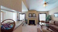 Located at 19321 Park Row Dr in Houston, TX 77084, this single-story residence offers a well-organized layout designed for comfortable living. The living room is a standout space, featuring soaring vaulted ceilings, a wood-burning fireplace with a classic white mantle, and multiple windows dressed with blinds and dark drape accents that allow for ample natural light. Carpeted flooring runs throughout the main living and bedroom areas, contributing to a warm and inviting ambiance. Adjacent to the living area is a dedicated dining space with a sliding glass door and window, providing a bright setting for meals. The galley-style kitchen is efficiently designed with granite-look countertops, a double stainless steel sink, white cabinetry, tile backsplash, and wood-look flooring, accommodating full appliances including a refrigerator and electric range. The space includes multiple bedrooms, each equipped with ceiling fans, carpeted floors, and access to closets. The bathrooms feature tub-shower combinations with tiled surrounds, granite-look countertops, and overhead cabinet storage. Overall, the space presents a cohesive, neutral color palette with warm beige tones throughout, offering a functional and comfortable living environment.