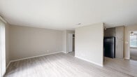This 2-bedroom, 1-bathroom unit in Birmingham, Alabama is designed with a clean, functional layout spread across a single floor. The living room is a generously sized open area featuring light wood-style luxury vinyl flooring and neutral warm-gray walls that create a bright, welcoming atmosphere. A large sliding glass door with vertical blinds allows natural light to pour in while offering views of the surrounding greenery outside. The kitchen is well-appointed with taupe cabinetry, granite-style countertops, a tile backsplash, and black appliances including a refrigerator and range, complemented by the same light flooring that runs throughout the main living areas. A carpeted hallway connects the private areas of the unit, leading to both bedrooms and the bathroom. The spacious primary bedroom includes a closet and continues the light flooring theme, while the second bedroom features plush carpet, a ceiling fan, and a window with outdoor views. The connecting hallway provides additional storage access and is lit by a recessed ceiling light, maintaining a tidy and organized flow between spaces. Clean white trim and consistent neutral wall colors throughout unify the overall aesthetic of this well-maintained unit.