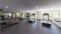 Located at 395 Brittany Farms Rd in the Normandy neighborhood of New Britain, Connecticut, this fitness center offers a well-equipped, single-floor exercise facility designed to support a comprehensive workout routine. The space is finished with durable rubber flooring throughout, providing both safety and comfort underfoot during exercise. Large windows line the walls, inviting abundant natural light and offering views of the surrounding greenery, creating an energizing atmosphere for workouts. Full-length wall mirrors are strategically positioned across multiple sections of the room, visually expanding the space and allowing users to monitor their form during exercise. The cardio zone features a row of treadmills and elliptical trainers from Life Fitness, catering to a range of aerobic training preferences. The strength training area is equipped with a multi-station cable machine, a weight bench, and additional resistance equipment, providing options for full-body conditioning. Recessed ceiling lighting supplements the natural light, ensuring the facility remains well-lit throughout the day. An open floor area offers flexible space for stretching, mat work, or bodyweight exercises. The overall design is clean, functional, and organized, making this fitness center a practical and inviting resource for regular use.