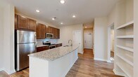Located at 1301 Charter Colony Pkwy in Midlothian, Virginia, this single-floor residence offers a well-designed layout with thoughtful finishes throughout. The kitchen serves as a central highlight, featuring rich espresso-toned cabinetry, a classic subway tile backsplash, stainless steel appliances — including a refrigerator, range, and microwave — and a generous granite-topped island with an integrated sink, providing ample prep and gathering space. Wood-look flooring flows through the kitchen and living areas, lending warmth and continuity to the open layout. The living room is bright and spacious, with natural light pouring in through a sliding glass door that opens onto a private outdoor balcony with exterior views. The bedrooms are finished with plush carpeting and feature large windows that invite natural light, along with closets offering generous storage. The bathroom includes a full soaking tub and shower combination with clean, neutral finishes. A dedicated in-unit laundry room houses a full-sized washer and dryer and is finished with tile flooring and louvered storage doors, adding everyday convenience. Throughout the residence, a neutral warm palette, recessed lighting, and consistent trim details create a cohesive and comfortable living environment.