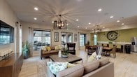 This single-floor community clubhouse is designed to offer a welcoming and versatile gathering space with a cohesive contemporary aesthetic throughout. The open-plan layout seamlessly connects multiple functional zones, all unified by large-format light stone tile flooring and an abundance of natural light streaming through numerous windows dressed with elegant drape curtains and adjustable blinds.

The main lounge area features generous seating arrangements with plush neutral sofas and accent chairs adorned with yellow and botanical-patterned throw pillows. Striking geometric chandelier light fixtures and recessed ceiling lighting illuminate the space warmly. A live-edge solid wood communal dining table serves as a centerpiece in the dining zone, surrounded by dark wood chairs and topped with a matching chandelier, offering an inviting setting for shared meals or gatherings.

Adjacent to the lounge, a dedicated recreation room provides a full-size billiards table, comfortable seating, and a wall-mounted flat-screen television, making it ideal for entertainment and socializing. The kitchenette area is appointed with dark wood cabinetry, a white quartz countertop, a stainless steel refrigerator, and a bar-height island with upholstered seating. Sage green accent walls and decorative oversized clock wall art add personality and warmth. Throughout the space, carefully placed indoor greenery enhances the fresh, inviting ambiance.