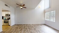 Located at 5917 N Oracle Rd in Tucson, Arizona, this two-story residence is thoughtfully laid out across two levels. The ground floor features an open living area with warm wood-look plank flooring, soaring vaulted ceilings, and large windows that invite abundant natural light. A striking spiral staircase with a sleek metal railing serves as both a functional and architectural centerpiece. The ceiling fan adds comfort suited to the Arizona climate. The galley-style kitchen is efficiently designed with white cabinetry, granite-look countertops, a stainless steel sink, dishwasher, refrigerator, and range, complemented by wood-look flooring that carries through from the main living area. A hallway connects to the bathroom, which features a full tub-shower combination with clean white surround and brushed nickel fixtures. Ascending to the upper level, a carpeted loft-style space is bright and airy, with a window overlooking the surroundings and open railing that overlooks the stairwell. A spacious walk-in closet on this floor offers built-in shelving, dual hanging rods, and carpeted flooring beneath a bold yellow ceiling accent, providing generous storage. The overall aesthetic is clean and neutral, presenting a functional and comfortable two-level living environment.