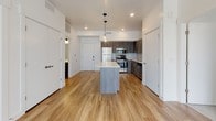 This single-floor unit features a contemporary design with a cohesive blend of modern finishes throughout. The open-concept kitchen and living area serves as the heart of the space, anchored by a central island with a clean white countertop and pendant lighting overhead. Dark wood-tone cabinetry lines the kitchen walls, complemented by a full suite of stainless steel appliances, including a refrigerator, gas range, and built-in microwave. Warm-toned hardwood-style flooring extends throughout the main living area, enhancing the bright, airy atmosphere created by recessed lighting.

Two bedrooms are finished with neutral carpeting, ceiling fans, and large windows fitted with horizontal blinds, allowing ample natural light while maintaining privacy. The bedrooms offer a calm, comfortable setting with clean white walls and generous proportions.

The bathrooms maintain the same modern aesthetic found throughout the unit. One features a full soaking tub with an integrated surround and built-in shelving, while the other is appointed with a wood-tone vanity, white countertop, large mirror, and brushed nickel fixtures. Wood-style flooring continues into the bathrooms, tying the overall design together cohesively.