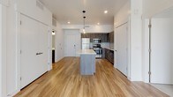 This single-floor unit features a contemporary design with a cohesive blend of modern finishes throughout. The open-concept kitchen and living area serves as the heart of the space, anchored by a central island with a clean white countertop and pendant lighting overhead. Dark wood-tone cabinetry lines the kitchen walls, complemented by a full suite of stainless steel appliances, including a refrigerator, gas range, and built-in microwave. Warm-toned hardwood-style flooring extends throughout the main living area, enhancing the bright, airy atmosphere created by recessed lighting.

Two bedrooms are finished with neutral carpeting, ceiling fans, and large windows fitted with horizontal blinds, allowing ample natural light while maintaining privacy. The bedrooms offer a calm, comfortable setting with clean white walls and generous proportions.

The bathrooms maintain the same modern aesthetic found throughout the unit. One features a full soaking tub with an integrated surround and built-in shelving, while the other is appointed with a wood-tone vanity, white countertop, large mirror, and brushed nickel fixtures. Wood-style flooring continues into the bathrooms, tying the overall design together cohesively.