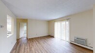 This single-floor unit offers a thoughtfully arranged layout encompassing a living room, kitchen, bedroom, closet, and full bathroom. The living room serves as the central gathering space, featuring light wood-style laminate flooring, neutral cream-toned walls, and a sliding glass door fitted with vertical blinds that allow abundant natural light and outdoor views. A ceiling fan and baseboard heating units are present throughout the unit, ensuring year-round comfort.

The kitchen is efficiently designed with white shaker-style cabinetry, dark granite-look countertops, a stainless steel sink, and white appliances including a full-size refrigerator and range, maximizing functionality within a compact footprint.

The bedroom provides a comfortable retreat, carpeted for warmth and featuring two windows that offer natural light and outdoor views. An adjoining built-in closet with shelving provides organized storage. A separate dedicated closet is also accessible within the unit.

The bathroom is clean and practical, equipped with a full tub-shower combination featuring built-in surround shelving, complemented by warm neutral tones throughout. Overall, the unit presents a bright, clean, and functional living environment.