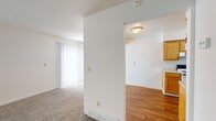 This two-story residence presents a practical and well-organized layout designed for comfortable everyday living. The main level opens into a spacious living area finished with neutral-toned carpet and fitted with vertical blinds that allow ample natural light to filter through large windows. A partial wall separates the living space from the adjoining areas, creating a sense of defined zones while maintaining an open feel. A floor-mounted heating vent ensures year-round comfort in this central space.

The galley-style kitchen is efficiently arranged with warm oak cabinetry lining both walls, offering generous upper and lower storage. Appliances include a coil-burner electric range, a black refrigerator, and a dishwasher, complemented by a stainless steel sink. Light hardwood-style flooring runs throughout the kitchen, and a door at the far end provides additional access. The kitchen connects seamlessly to an adjacent dining or entry area, also finished in hardwood-style flooring.

The bedrooms are carpeted and bright, each featuring windows with vertical blinds that bring in natural light. One bedroom includes a ceiling fan with a light fixture. The bathroom is cleanly appointed with tile flooring, a full tub-shower combination, a wood-tone vanity with a white countertop, and brushed nickel grab bars for added convenience.
