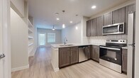 This efficiently designed 1-bedroom, 1-bathroom residence offers a thoughtful single-floor layout that maximizes every square foot. The open-concept kitchen flows seamlessly into the living area, creating a bright and connected living space. The kitchen is a standout feature, equipped with stainless steel appliances including a refrigerator, electric range, over-the-range microwave, and dishwasher. Rich dark walnut-toned cabinetry is complemented by granite countertops and a classic white subway tile backsplash. A peninsula with pendant lighting above provides additional workspace and serves as a natural divider between the kitchen and living area. Light wood-style plank flooring runs throughout the main living areas, adding warmth and continuity. The living room benefits from natural light through a large window and glass door, with a ceiling fan overhead. The bedroom offers comfortable carpeted flooring, a ceiling fan, and a window with exterior views. The bathroom is well-appointed with matching dark cabinetry, granite countertop, a large vanity mirror with overhead lighting, tile flooring, and direct access to a walk-in closet. A hallway connects the private and common areas, completing this cohesive and modern layout.