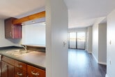 Located at 717 Seventh St in downtown Des Moines, Iowa, this two-bedroom, one-bathroom unit offers a practical and well-organized single-floor layout. A welcoming entrance opens into a bright hallway with hardwood-style flooring that flows throughout the main living areas. The open-concept living room is spacious and filled with natural light, anchored by a large sliding glass door that leads to a private balcony with views of the surrounding cityscape. The kitchen sits adjacent to the living area in a galley-style configuration, featuring warm wood cabinetry, dark countertops, stainless steel appliances including a range and over-the-range microwave, a black refrigerator, and a double basin sink — all oriented around an efficient corridor layout. The primary bedroom offers generous proportions and direct outdoor views through a large window. The second bedroom is finished with plush carpet and features warm wood-tone doors, adding a cozy contrast to the neutral walls. Three closets throughout the unit provide ample storage. The bathroom includes a full tub-shower combination with clean white fixtures. Neutral tones and consistent finishes throughout create a cohesive and functional living environment suited for everyday comfort.