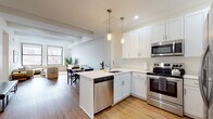 This single-floor residence offers a thoughtfully designed layout that blends modern finishes with a warm, inviting atmosphere. The open-concept kitchen is a standout feature, equipped with crisp white shaker cabinetry, quartz countertops, a peninsula island, pendant lighting, and a full suite of stainless steel appliances including a dishwasher, electric range, microwave, and French door refrigerator. Hardwood flooring flows seamlessly from the kitchen into the dining and living areas. The living room is generously proportioned, featuring exposed beam detailing on the ceiling, large black-framed windows that invite abundant natural light and treetop views, and recessed lighting overhead. Two well-sized bedrooms provide comfortable retreats, each finished with the same warm hardwood floors, clean white walls, and ample natural light — one benefiting from a dedicated window with exterior views. The bathroom is elegantly appointed with large-format marble-look tile flooring, white subway tile walls, a white vanity with a marble countertop, and a wall mirror. Throughout the residence, a neutral palette and clean architectural lines create a cohesive and contemporary aesthetic ideal for modern living.