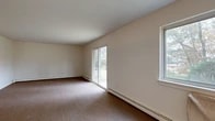 Located at 18 Scenic Dr in Croton-on-Hudson, NY, this single-floor, two-bedroom, one-bathroom residence offers a practical and straightforward layout across a comfortable footprint. The combined living and dining area is a standout space, featuring carpet flooring, baseboard heating, and a sliding glass door that opens to views of the surrounding tree-lined landscape, alongside an additional window that draws in natural light. A central hallway connects the main rooms, lined with sliding wood-paneled closet doors — one of an impressive seven closets distributed throughout the unit, ensuring ample storage. The kitchen is efficiently designed with warm wood cabinetry, granite-style countertops, open corner shelving, a stainless steel sink beneath a window overlooking the greenery outside, and a gas range. The spacious primary bedroom offers generous proportions and a large sliding-door closet, while the second bedroom is well-sized with access to additional closet space. The bathroom features full white tile surround, a soaking tub, and a window for natural ventilation. Baseboard heating is present throughout. The outdoor setting features mature trees and seasonal foliage, contributing to the scenic, nature-adjacent character of the property.