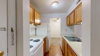 This 2-bedroom, 2-bathroom residence in Maryland Heights, Missouri, offers a practical and well-organized single-floor layout. The galley-style kitchen features warm honey-toned wood cabinetry, light countertops, a double-coil electric range, a full-size refrigerator, and a stainless steel sink — all set over hardwood-style flooring. The kitchen opens into the adjoining dining and living areas, where a ceiling fan adds comfort and a sliding glass door leads to a private balcony with outdoor views. The living room is carpeted and filled with natural light. Both bedrooms are carpeted and feature windows with horizontal blinds that allow for natural light and privacy. The spacious primary bedroom includes generous closet space with sliding panel doors. Additional storage is well-represented throughout, with four closets distributed across the floor plan. The two bathrooms are clean and functional — one includes a glass-enclosed shower stall with hardwood-style flooring, while the other features a full soaking tub and shower combination with bright white surround panels. A dedicated utility room and a hallway round out the interior. The neutral color palette throughout creates a bright, move-in-ready atmosphere.