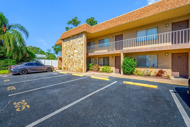 Charming two-story apartment building with a stone facade, surrounded by lush greenery and ample parking space, under a clear blue sky. - Parkview Apartments