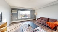 Located at 515 E Grant St in Minneapolis, this 2-bedroom, 1-bathroom unit offers a well-designed layout across a single floor. The open living area is bright and welcoming, featuring wood-style plank flooring, neutral gray walls, and large windows that frame sweeping views of the Minneapolis skyline. A wall-mounted AC unit ensures year-round comfort, while baseboard heating runs along the exterior walls.

The kitchen is thoughtfully appointed with white shaker-style cabinetry, dark countertops, stainless steel appliances including a refrigerator, dishwasher, and range, and durable wood-style flooring that ties seamlessly into the adjacent dining and living spaces.

Both bedrooms are carpeted and filled with natural light. The generously sized primary bedroom offers city views through a large sliding window, along with dual closets featuring built-in shelving for ample storage. The second bedroom mirrors the same bright, airy feel.

The bathroom is finished with a white shaker vanity, white countertop, a large framed mirror, and rich wood-style tile flooring, accented by a bold gray feature wall. Two hallways connect the rooms efficiently, adding to the unit's functional flow. Dedicated closet space and multiple hallway connections enhance the overall practicality of this Minneapolis residence.