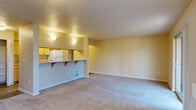 This single-floor, 2-bedroom, 1-bathroom residence offers a practical and comfortable layout designed for everyday living. The combined kitchen and living room serves as the heart of the home, featuring a peninsula-style breakfast bar with bracket shelving that separates the kitchen from the carpeted living area. The kitchen is equipped with light wood cabinetry, a white refrigerator, electric range, and microwave, complemented by wood-look vinyl flooring. A dedicated laundry area with a full-size washer and dryer is conveniently located just off the kitchen. The spacious living room is bathed in natural light through large sliding glass doors and an adjacent window, both offering views of surrounding greenery. The primary bedroom is generously sized with a window and direct access to a walk-in closet outfitted with wire shelving and hanging rods. The second bedroom also features carpeting, a window with natural light, and closet access. The full bathroom includes vinyl wood-look flooring, a vanity, and a built-in towel bar. Throughout, warm beige and neutral tones create a clean, cohesive aesthetic, while carpet in the living and bedroom areas adds comfort underfoot.