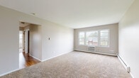 Located at 606 Ivarene Ct in Carpentersville, Illinois, this single-floor unit offers a straightforward and functional layout designed for comfortable everyday living. The spacious living room is finished with neutral-toned carpet and features a large multi-pane window that fills the room with natural light and frames views of surrounding greenery. A baseboard heating unit and wall-mounted air conditioner ensure year-round comfort. Adjacent to the living area, an entry room with carpet flooring provides a welcoming transition into the home, complete with its own window and exterior door. The kitchen is equipped with warm oak cabinetry, white countertops, a gas range with overhead ventilation, and a double-basin stainless steel sink, all set atop wood-look flooring. The bedrooms are generously sized, featuring plush carpeting, neutral walls, and windows that offer outdoor views — one room includes hardwood-style flooring and a serene lawn view. Additional rooms include a carpeted bedroom with a walk-in closet. The full bathroom includes a wood-toned vanity with a single sink, a lighted mirror, a shower-tub combination, and wood-look flooring. Baseboard heating is consistent throughout the home, contributing to a clean and cohesive interior.