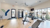 The Yardly Eden fitness center at 1841 Mansfield Webb Road in Arlington, Texas, is a thoughtfully designed exercise facility offering a comprehensive workout experience in a clean, modern setting. The single-room space features light hardwood-style flooring, crisp white walls, and elevated ceilings that lend an open, airy feel throughout.

Natural light floods the interior through large floor-to-ceiling windows along one wall, offering views of the surrounding neighborhood and creating a bright, energizing atmosphere. A ceiling fan overhead ensures comfortable airflow during workouts, while recessed lighting provides even illumination throughout the space.

The facility is well-equipped for a full range of fitness activities. Cardio equipment includes treadmills, a rowing machine, a stationary bike, and an elliptical trainer, each positioned to take advantage of the outdoor views. For strength training, the room offers a multi-functional cable machine, an adjustable weight bench, and an extensive dumbbell rack with a full range of free weights. Stability balls and additional accessories are neatly organized on a dedicated storage rack.

A wall-mounted flat-screen television adds entertainment options during workouts. The Yardly branding is prominently displayed on a feature wall, reinforcing the space's identity. A water fountain and a sanitation station are conveniently available, and branded entry mats complete the polished, community-focused aesthetic.