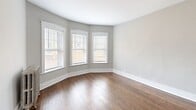 Located at 2000-2006 W Fargo Ave in Chicago's Rogers Park neighborhood, this 2-bedroom, 1-bathroom unit combines classic architectural character with modern updates. Rich dark hardwood floors run throughout the entire space, complemented by neutral gray walls and crisp white trim that create a clean, cohesive aesthetic.

The updated kitchen features white shaker-style cabinetry, white countertops, and stainless steel appliances including a gas range and dishwasher. A window provides natural light, making the space feel bright and functional.

The living room is a standout, boasting a graceful curved bay window arrangement with three windows that flood the room with natural light and lend a distinctive architectural charm. Both bedrooms are well-proportioned, with the primary bedroom offering ample space. Each bedroom features windows with blinds and classic cast-iron radiators that add vintage character while providing efficient heat. The hallway connects the rooms efficiently, with closets flanking either side for generous storage.

The bathroom is clean and bright, finished with light tile surround and a full soaking tub with a window above. Throughout the unit, six-panel white doors and arched doorway trim details reflect the building's timeless Chicago architecture.