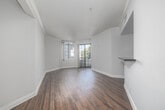 Located on Burton Way in Los Angeles, CA, this single-floor unit offers a thoughtfully designed layout that maximizes its efficient footprint. The space is entered through a hallway distinguished by elegant arched doorways, recessed lighting, and rich hardwood flooring that flows throughout the main living areas.

The open kitchen and living room configuration forms the heart of the unit. The kitchen is outfitted with stainless steel appliances — including a French door refrigerator, gas range, built-in microwave, and dishwasher — complemented by rich dark wood cabinetry, dark granite countertops, and a teal glass tile backsplash. Light hardwood flooring adds warmth to the kitchen area.

The living room is bright and airy, featuring crown molding, neutral tones, and dark hardwood floors. A large arched window along with a full-height steel-framed glass door floods the space with natural light and provides access to an outdoor area with views of surrounding greenery.

The bathroom is well-finished, showcasing warm beige tile flooring and walls, a vessel sink atop a dark wood vanity with a granite countertop, and a full tub with sliding glass shower doors. A dedicated closet provides convenient storage. This unit combines classic architectural charm with modern finishes throughout.
