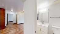 Located at 1101 Howard Street, Unit 403, in San Francisco's SoMa neighborhood, this three-bedroom, two-bathroom residence offers a functional and well-designed single-floor layout. Warm-toned hardwood flooring runs throughout the living areas and bedrooms, creating a cohesive and inviting atmosphere. The combined kitchen and living room area serves as the heart of the home, featuring a ceiling fan, ample natural light from a large window, and direct sightlines to the bedrooms. The kitchen is outfitted with rich, medium-toned wood cabinetry, granite-style countertops, a full suite of white appliances, and generous storage extending to the ceiling. Each of the three bedrooms is bright and well-proportioned, with large windows framing views of the surrounding urban landscape and mature street trees. Baseboard heating is present throughout. The primary bedroom offers a comfortable footprint with city views. Both bathrooms are finished with neutral tile flooring, white vanities featuring clean-lined cabinetry, and chrome fixtures. One bathroom includes a full soaking tub with an overhead shower and tiled surround, while the second offers a streamlined vanity and toilet configuration. A hallway and closet complete the layout, providing practical storage and connectivity between rooms.