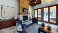 Located at 1105 Sharview Circle in Charlotte, NC, this single-floor commercial space presents a polished and welcoming environment with high-end architectural finishes throughout. The grand entrance features rich wood-paneled walls, a decorative bubble chandelier, and striking stone tile flooring with inlaid dark accent patterns — setting a sophisticated tone from the moment of arrival. Glass-flanked entry doors allow natural light to pour into the vestibule, offering views of the surrounding greenery outside.

The interior opens into a spacious lounge and gathering area defined by soaring wood-beamed coffered ceilings and a dramatic floor-to-ceiling stone fireplace surround with a mounted flat-screen television above the mantel. Built-in dark wood cabinetry flanks the fireplace, providing functional storage and display space. Comfortable seating is arranged throughout the lounge, creating an inviting atmosphere for conversation and relaxation.

French doors along the rear wall open directly to an outdoor area, flooding the interior with natural light and providing seamless indoor-outdoor connectivity. The transition zone between the entrance and lounge features recessed lighting, white walls, and framed display niches, balancing warmth with a clean, contemporary aesthetic. Overall, the space combines classic craftsmanship with modern comfort in a professional, community-oriented setting.