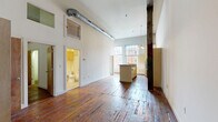 Located on West Broad Street in Richmond, Virginia, this 2-bedroom, 2-bathroom loft-style unit blends historic industrial character with modern functionality. The open-concept main living area immediately impresses with dramatically high ceilings, exposed ductwork, and a prominent original timber beam that speaks to the building's storied past. Richly toned original hardwood floors run throughout, adding warmth and texture to the space.

The kitchen features a center island with granite countertops, light maple cabinetry reaching toward the tall ceilings, and stainless steel appliances including a refrigerator and over-the-range microwave. A white-painted exposed brick accent wall and large windows allow natural light to pour into the living area, offering views of the surrounding streetscape.

Both bedrooms continue the hardwood flooring and benefit from the unit's generous ceiling heights. One bedroom showcases a striking white-painted brick wall, while the other includes a closet and in-unit stacked washer and dryer. Each room maintains a clean, neutral palette.

The two bathrooms are finished with tile flooring and light maple cabinetry. One features a pedestal sink, and the other includes a full tub-shower combination. Two closets provide additional storage throughout the unit.