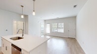 Located at 44000 Owl Wood Lane in Summerville, SC, this one-bedroom, one-bathroom residence offers a thoughtfully designed single-floor layout with clean, contemporary finishes throughout. The open-concept living and kitchen area is bright and airy, featuring light hardwood-style flooring, white walls, and large windows fitted with blinds that allow ample natural light to fill the space. The kitchen is well-appointed with white shaker-style cabinetry extending to the ceiling, a white quartz countertop island with pendant lighting overhead, and a full suite of stainless steel appliances including a refrigerator, electric range, microwave, and dishwasher. A white subway tile backsplash adds a polished touch. The living room offers a comfortable, open feel with additional windows providing outdoor views. The bedroom features soft carpet flooring, a ceiling fan, and a window with natural light. The bathroom is finished in white with a single-sink vanity, white cabinetry, wood-look tile flooring, and a full tub and shower combination with white subway tile surround. A dedicated laundry room houses a full-size washer and dryer with overhead wire shelving for added storage. A closet completes the layout, offering practical everyday convenience.