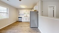 Located at 1600 W Arlington Blvd in Greenville, North Carolina, this single-floor unit offers a clean, contemporary aesthetic with thoughtful updates throughout. The kitchen serves as a functional centerpiece, outfitted with crisp white cabinetry accented by matte black hardware, a classic white subway tile backsplash, stone-look countertops, and a full suite of stainless steel appliances including a refrigerator, electric range, and dishwasher. A double-basin sink completes the well-organized workspace, making the kitchen both practical and visually appealing. The open layout connects the kitchen to the living area, which benefits from a bright, airy feel enhanced by neutral wall tones and durable wood-look flooring that extends seamlessly across the space. The bedroom offers a comfortable, understated setting with the same consistent flooring and soft natural light. The bathroom features a white vanity topped with a striking marble-look countertop and undermount sink, complemented by matte black fixtures and a large wall mirror. Neutral gray walls and the wood-look flooring tie the bathroom's design together cohesively. A louvered closet door visible from the bathroom adds functional storage nearby. Throughout, the space presents a fresh, move-in-ready condition with a consistent modern design palette.