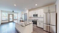 Located at 3812 W Montague Ave in North Charleston, SC, this well-appointed one-bedroom, one-bathroom residence offers a thoughtfully designed single-floor layout that maximizes every square foot of its compact footprint. The open-concept kitchen serves as the centerpiece of the living space, showcasing a striking granite-topped island with an undermount sink and matte black faucet, crisp white cabinetry, a hexagonal tile backsplash, and a full suite of stainless steel appliances including a gas range, built-in microwave, and French door refrigerator. Wood-look plank flooring flows seamlessly throughout the entire unit, lending warmth and visual continuity. The living area benefits from natural light through large windows, creating a bright and open atmosphere. The bedroom is a comfortable, well-proportioned space featuring a ceiling fan, a large window with outdoor views, and access to a dedicated closet. The bathroom offers a clean, modern aesthetic with a granite-topped vanity, black hardware accents, and a separate water closet with additional storage access. Recessed lighting and neutral wall tones throughout contribute to a fresh, contemporary ambiance suited for everyday living.