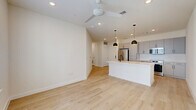 Located at 1614 N St Marys St in San Antonio, TX, this thoughtfully designed one-bedroom, one-bathroom unit offers a clean, modern aesthetic across a single floor. The open-concept living and kitchen area is anchored by light-toned hardwood flooring, recessed lighting, and a ceiling fan that enhances airflow and comfort. The kitchen is a standout feature, equipped with stainless steel appliances including a refrigerator, electric range, and over-the-range microwave. Sleek gray flat-front cabinetry, white subway tile backsplash, and a white quartz countertop island with a matte black faucet and undermount sink complete the contemporary look. Stylish black pendant lights hang above the island, adding a striking contrast. The living area benefits from natural light through a large window. The bedroom is carpeted for comfort, fitted with a ceiling fan, and connected to a well-organized walk-in closet with built-in shelving and hanging rods. The bathroom features light hardwood-style flooring, a gray vanity with white countertop, matte black fixtures, a large mirror, and a glass-enclosed walk-in shower with tile surround. Additional utility rooms and closets provide practical storage throughout.