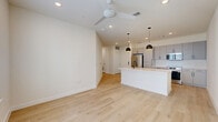 Located at 1614 N St Marys St in San Antonio, TX, this thoughtfully designed one-bedroom, one-bathroom unit offers a clean, modern aesthetic across a single floor. The open-concept living and kitchen area is anchored by light-toned hardwood flooring, recessed lighting, and a ceiling fan that enhances airflow and comfort. The kitchen is a standout feature, equipped with stainless steel appliances including a refrigerator, electric range, and over-the-range microwave. Sleek gray flat-front cabinetry, white subway tile backsplash, and a white quartz countertop island with a matte black faucet and undermount sink complete the contemporary look. Stylish black pendant lights hang above the island, adding a striking contrast. The living area benefits from natural light through a large window. The bedroom is carpeted for comfort, fitted with a ceiling fan, and connected to a well-organized walk-in closet with built-in shelving and hanging rods. The bathroom features light hardwood-style flooring, a gray vanity with white countertop, matte black fixtures, a large mirror, and a glass-enclosed walk-in shower with tile surround. Additional utility rooms and closets provide practical storage throughout.