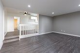 Located at 12122 Harbor Blvd in Garden Grove, California, this single-floor unit offers a clean, modern aesthetic with thoughtful finishes throughout. The open living area is finished with durable wood-look plank flooring and neutral warm-gray walls, creating a versatile and welcoming atmosphere. Recessed lighting illuminates the space efficiently, while a wall-mounted air conditioning unit and vertical blinds on a large window provide comfort and light control. A ceiling fan adds to the functional design in an adjacent area, which features a classic white-railed staircase detail and additional recessed lighting. The kitchen is a standout feature, outfitted with crisp white cabinetry, sleek quartz-style countertops, a subway tile backsplash, and a full suite of stainless steel appliances including a range, over-the-range microwave, and a stainless sink — ideal for everyday cooking. The bathroom is equally polished, showcasing white shaker-style cabinetry, a wide vanity with an integrated oval sink, a decorative framed mirror, and a separate water closet with a full shower-tub combination. Wood-look flooring carries through into the bathroom, tying the space together cohesively. This unit presents a well-maintained, move-in-ready interior with a consistent modern design language throughout.