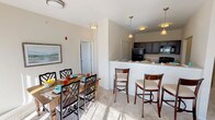This single-floor residence offers a thoughtfully designed open-concept layout that seamlessly connects the kitchen, dining, and living areas. The kitchen is equipped with dark espresso cabinetry, granite-style countertops, black appliances including a refrigerator, electric range, and built-in microwave, and durable hardwood-style flooring. A raised breakfast bar with pendant lighting provides additional seating and serves as a natural divider between the kitchen and dining space, where a full dining table comfortably accommodates multiple guests.

The living area features plush carpeting and neutral walls that create a warm, versatile backdrop. Two well-proportioned bedrooms are bathed in natural light from large windows with exterior views, and both feature soft carpet flooring. The primary bathroom offers a dual-sink vanity with granite-style countertops, stylish cabinetry, and direct access to a walk-in closet with built-in shelving. A secondary bathroom includes a tub-shower combination with clean white fixtures. Throughout the residence, consistent neutral tones, flush-mount and pendant lighting, and quality finishes contribute to a cohesive, comfortable ambiance.