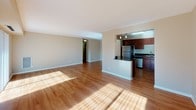 This single-floor residence offers a well-organized layout that balances open communal areas with functional private spaces. The living area is expansive and sun-drenched, with warm hardwood-style flooring that runs throughout the main areas and a sliding glass door alongside a large window that invites abundant natural light and provides outdoor views of surrounding greenery. Neutral-toned walls complement the bright, airy atmosphere.

The kitchen is thoughtfully designed, featuring rich dark wood cabinetry extending to the upper walls for ample storage, dark granite countertops, and a suite of stainless steel appliances including a gas range with overhead microwave, refrigerator, and dishwasher. A peninsula counter separates the kitchen from the living area, creating a natural open-concept flow enhanced by track lighting overhead.

The bedroom offers hardwood-style flooring, a window with outdoor views, and a double closet system with built-in shelving, providing practical and generous storage solutions.

The bathroom is finished with large-format tile flooring, a wide vanity with an extended mirror, wood cabinetry with drawer storage, and a tiled tub-shower combination, delivering a clean and functional design throughout.