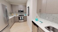 This single-floor, 2-bedroom, 2-bathroom residence offers a thoughtfully designed layout with contemporary finishes. The kitchen is a standout feature, showcasing sleek gray cabinetry with brushed nickel hardware, crisp white quartz countertops, and a mosaic tile backsplash that adds visual texture to the space. Stainless steel appliances — including a gas range, built-in microwave, and dishwasher — provide a polished, functional cooking environment. Light wood-tone flooring runs throughout, lending warmth and continuity to the space. The kitchen is configured in an efficient galley-style layout, maximizing counter and storage space while maintaining an open, uncluttered feel. Neutral white walls keep the interior bright and versatile, complementing the modern aesthetic of the cabinetry and fixtures. The overall design balances practicality with contemporary style, making it well-suited for everyday living. With two bedrooms and two full bathrooms, the residence offers comfortable accommodations for a variety of living arrangements.