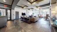 This single-floor communal space is thoughtfully designed to offer a range of functional and social environments under one roof. Throughout, large-format slate tile flooring provides a cohesive, upscale foundation, while coffered ceilings with recessed lighting add architectural depth and a sense of grandeur.

The kitchen is a standout feature, outfitted with slate-blue cabinetry, white quartz countertops, stainless steel appliances including a built-in double oven and French door refrigerator, and a substantial center island. Oversized windows flood the space with natural light and offer views of an outdoor pool area.

The main lounge area is anchored by a seating arrangement with a wall-mounted television, complemented by large windows that bring in abundant daylight. Structural columns define the open layout without interrupting sightlines. Adjacent to this is a game room with billiards, dining-height tables, bar seating, and additional television displays.

A private seating nook features a high-back booth and accent chairs, offering a quieter retreat. A corridor-style area provides a wall-mounted screen and counter workspace, leading to a glass-door conference room, ideal for meetings or focused work.