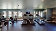 Located at 10757 Lemon Ave in Rancho Cucamonga, California, this well-equipped fitness center offers a comprehensive workout environment designed to accommodate a wide range of exercise routines. The single-floor facility is finished with durable rubber flooring throughout, providing a safe and cushioned surface ideal for both cardio and strength training activities.

The cardio area is lined with a row of Spirit-brand treadmills and elliptical machines, positioned to face large windows that look out onto lush, tree-lined surroundings, creating an energizing atmosphere during workouts. Multiple flat-screen televisions are mounted on the walls, keeping users entertained throughout their sessions.

The strength training section features a tiered dumbbell rack stocked with a full range of free weights, accompanied by adjustable weight benches for versatile lifting exercises. A cable resistance machine and additional selectorized strength equipment round out the selection, supporting full-body training. Full-length wall mirrors reflect the space, enhancing the open feel of the room and aiding in proper form during exercises.

Recessed lighting illuminates the interior evenly, while the soft blue-gray walls contribute to a calm, focused ambiance. Glass-panel doors provide an elegant entry point into the facility, adding a polished, modern touch to the overall design.