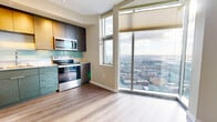 This 420 square foot studio apartment in Seattle showcases a modern, open-concept design that maximizes space efficiency. The interior features light-colored hardwood flooring throughout, creating a seamless flow between living areas. A standout architectural element is the exposed concrete column, adding an industrial touch to the otherwise contemporary space.

The kitchen is a highlight, boasting sleek two-tone cabinetry in wood grain and gray finishes. It's equipped with stainless steel appliances, including a full-size refrigerator, oven with stovetop, microwave, and dishwasher. A light blue glass backsplash adds a subtle pop of color, while quartz countertops provide ample workspace.

Large windows flood the space with natural light and offer city views, enhancing the sense of openness. The living area is versatile, with room for a bed and small seating arrangement. A sliding partition wall allows for privacy when needed.

While not visible in the images, the apartment includes a full bathroom. The overall design emphasizes clean lines, neutral tones, and modern fixtures, creating a stylish and functional living space in the heart of Seattle.
