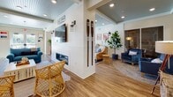 Located at 50 Perkins Farm Drive in Stonington, Connecticut, this thoughtfully designed single-floor community space embraces a vibrant coastal aesthetic throughout. The open lounge area serves as the heart of the space, featuring a sleek linear fireplace, beadboard ceiling painted in a soft seafoam tone, and warm hardwood-style flooring. Nautical accents — including decorative oars, coral wall art, a mounted marlin, and a nod to nearby Mystic, CT — lend the space an inviting, seaside character. Comfortable rattan and upholstered seating arrangements create distinct conversation areas, while lush indoor greenery adds a natural touch.

The kitchen is well-appointed with white shaker cabinetry, granite-style countertops, teal subway tile backsplash, and stainless steel appliances. A beadboard ceiling continues the coastal theme, and glass French doors open directly to an outdoor patio and gazebo, filling the kitchen with natural light and seamless indoor-outdoor flow.

Multiple dining areas offer flexible seating, highlighted by charming sailboat-patterned wallpaper paired with white wainscoting. Additional smaller rooms with textured wallcoverings provide intimate settings for private gatherings. Together, these spaces create a warm, community-focused environment with distinctive coastal charm.