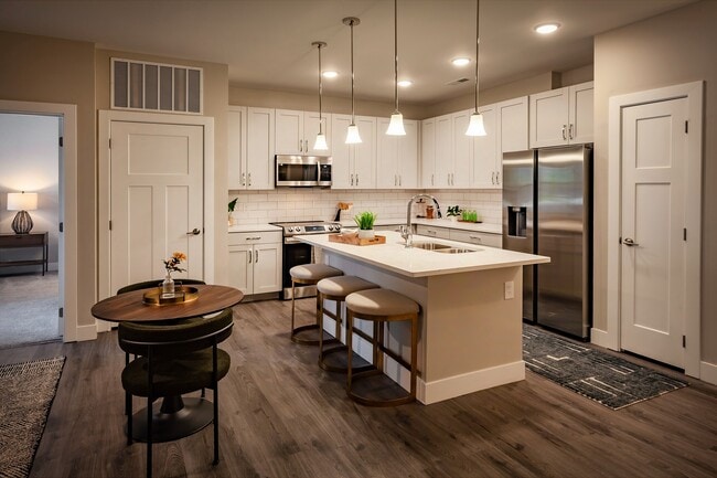 Modern apartment kitchen featuring white cabinetry, pendant lighting, stainless steel appliances, and a spacious island with bar seating for entertaining. - Madison at Greenwood