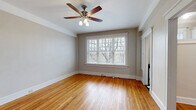 Located on Madison Avenue in Memphis, Tennessee, this efficiently designed single-floor unit offers a thoughtfully arranged layout comprising a living room, kitchen, bathroom, and closet. The living room is a standout space, showcasing warm-toned hardwood floors that run throughout, neutral taupe walls, and a large multi-pane window fitted with white blinds that floods the room with natural light and frames views of surrounding trees. A ceiling fan with a built-in light fixture anchors the room, while a wall-mounted mini-split unit provides climate control. The kitchen features dark stone countertops, white cabinetry, a classic bridge-style faucet in brushed brass, and a deep stainless steel sink positioned beneath a window, offering both function and natural light. A bold blue tile backsplash adds a distinctive design touch. The bathroom is a striking composition of classic black square wall tiles contrasted against white hex mosaic floor tiles, a pedestal sink, a full tub-shower combination, and a recessed medicine cabinet with vanity lighting — evoking a timeless vintage aesthetic. The closet provides dedicated storage, completing this compact yet characterful unit in the heart of Memphis.