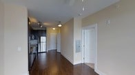 Located at 700 Spring Falls Dr in Raleigh, NC, this single-floor residence offers a well-designed layout that balances comfort and functionality. The space is anchored by rich, dark hardwood flooring that flows seamlessly throughout the main living areas, adding warmth and a sense of continuity to the interior.

The kitchen is equipped with stainless steel appliances, including a full-sized refrigerator and range, complemented by dark cabinetry that provides ample storage while contributing to a sleek, modern aesthetic. Track lighting overhead ensures the kitchen is well-lit and practical for everyday use.

A hallway connects the main living area to the rest of the residence, lined with white-paneled doors and finished with warm, neutral-toned walls that create a bright and welcoming atmosphere. Pendant lighting fixtures hang along the corridor, adding a touch of character to the transitional spaces. An electrical panel is thoughtfully recessed into the wall, maintaining the clean lines of the interior.

The overall ambiance is contemporary and inviting, with a cohesive design palette of dark floors, warm beige walls, and white trim that lends the space a polished, move-in-ready appeal. The single-floor plan ensures easy accessibility and efficient use of space throughout.