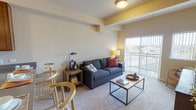 This single-floor residence offers a thoughtfully designed layout across two bedrooms and two full bathrooms. The living room serves as a central gathering space, featuring carpeted flooring, decorative ceiling beams with yellow accent detailing, and a sliding glass door that opens to a private balcony with open outdoor views, allowing natural light to fill the room.

The kitchen is efficiently arranged with warm-toned wood cabinetry extending to the ceiling for generous storage, a stainless steel sink set into a peninsula-style counter, and white appliances including a range, microwave, and refrigerator. The peninsula doubles as a casual dining area.

Both bedrooms are carpeted and receive natural light through large windows with outdoor views. Each room offers comfortable proportions, and at least one bedroom includes a walk-in closet with built-in wire shelving for organized storage.

The two bathrooms each feature wood-tone cabinetry, light countertops, and light hardwood-style flooring. One bathroom includes an extended vanity with wall-mounted cabinetry above, while the other offers a shower-tub combination. Together, the rooms create a cohesive, functional living environment with a neutral, welcoming palette throughout.