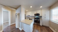 Located at 20435 Santa Maria Ave in Castro Valley, California, this single-story home presents a well-maintained interior with thoughtfully updated finishes throughout. The open-concept kitchen serves as a central highlight, featuring crisp white shaker cabinetry extending to the ceiling for generous storage, light stone countertops, a peninsula with additional workspace, and a full suite of stainless steel appliances including a gas range, over-the-range microwave, and dishwasher. Recessed lighting and a window with blinds bring natural light into the kitchen, enhancing its clean, modern aesthetic. Rich wood-look flooring runs through the kitchen and living areas, providing a warm and cohesive look. The living area is open and comfortable, with a ceiling fan and a window that allows natural light to fill the space. Bedrooms offer ceiling fans and windows with blinds; select rooms feature the same wood-look flooring while others are finished with plush carpeting for added comfort. The bathroom is neatly appointed with a white vanity, tub-shower combination, a large mirror, and coordinating hardware, all finished with wood-look flooring for continuity. Neutral wall tones throughout create a calm, versatile backdrop well-suited to a variety of interior styles.
