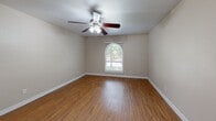 Located at 4046 Woodland Park Blvd in Arlington, TX, this single-story, 3-bedroom, 2-bathroom home offers a practical and comfortable layout with consistent warm-toned hardwood-style flooring throughout. The open living and dining area is anchored by a charming pendant light and a large window with blinds that invites natural light into the space. An arched window in the living room adds a distinctive architectural touch while framing views of the surrounding greenery. The kitchen features white cabinetry, white appliances including a refrigerator and electric range, and a pass-through counter that connects it to the main living area, making it ideal for everyday functionality. Each of the three bedrooms is well-proportioned, with ceiling fans providing comfort and arched or standard windows allowing natural light. The spacious primary bedroom includes a generous walk-in closet fitted with dual hanging rods and hardwood-style flooring, offering ample storage. The bathrooms are clean and functional, with one featuring a full tub and shower combination surrounded by white tile. Neutral beige walls and white trim run throughout the home, creating a cohesive and move-in-ready aesthetic. A hallway connects the bedrooms and bathrooms, contributing to a logical and efficient floor plan.