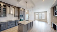 Located at Aspen Grove Dr in Franklin, TN, this well-appointed 2-bedroom, 2-bathroom residence offers a thoughtfully designed single-level layout with modern finishes throughout. The open-concept kitchen and living area serves as the heart of the home, anchored by a large center island with a quartz countertop, an undermount sink, and sleek slate-blue cabinetry that extends to the ceiling for ample storage. Pendant lighting and stainless steel appliances, including a French door refrigerator and double wall ovens, complete the polished culinary space. Light hardwood flooring flows through the main living areas, while a recessed tray ceiling adds architectural interest above the kitchen. The primary bedroom features plush carpeting, a ceiling fan, and multiple windows that invite natural light and outdoor views. Its ensuite bathroom impresses with a dual-sink vanity topped in white quartz, marble-look tile flooring, and a glass-enclosed walk-in shower dressed in floor-to-ceiling marble-style tile with a built-in bench. A spacious walk-in closet with multi-tiered shelving and hanging rods provides generous storage. The second bedroom is equally well-lit and carpeted, served by a second full bathroom. A private balcony extends the living space outdoors, offering open views of Franklin's dynamic urban landscape.