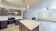 Located in Colorado Springs, CO, this well-designed one-bedroom, one-bathroom residence offers a thoughtfully planned open-concept layout with modern finishes throughout. Light wood-style flooring flows across the main living areas, complementing the neutral color palette and creating a bright, cohesive atmosphere.

The kitchen is a standout feature, showcasing rich dark cabinetry with sleek hardware, white quartz countertops, a full suite of stainless steel appliances including a refrigerator, electric range, dishwasher, and built-in microwave, and a central island with pendant lighting above. Track lighting and ample cabinetry provide both functionality and style.

The open living room is filled with natural light from a large window, features a ceiling fan, and includes a wall-mounted fireplace, with access to a patio or balcony via a sliding door. The bedroom offers plush carpeting, a ceiling fan, and a dedicated window for natural light. Adjacent is a walk-in closet with wire shelving systems for organized storage.

The bathroom is finished with a dark vanity, white quartz countertop, an illuminated mirror, and a full tub/shower combination with brushed nickel fixtures. A convenient hallway connects all spaces, completing this clean and functional floor plan.